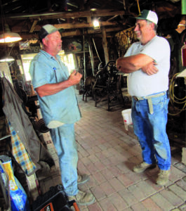 Two men talk to each other in the blacksmithing shop.